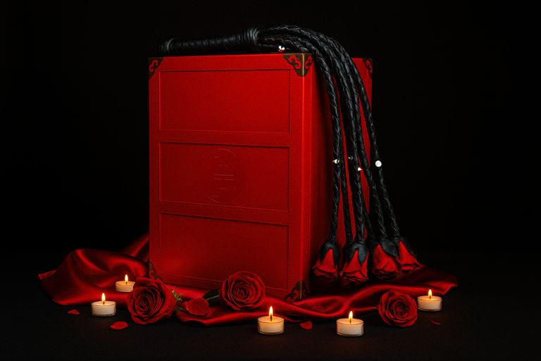 Sinnliche BDSM-Box mit schwarzer Peitsche auf rotem Hintergrund