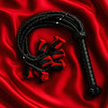 Luxuriöse BDSM Peitsche, künstlerisch arrangiert auf rotem Hintergrund.